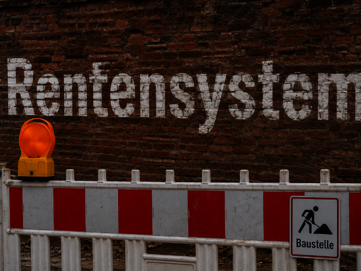 Das Bild zeigt eine Mauer mit dem Schriftzug Rentensystem, davor steht eine Baustellenabsperrung.